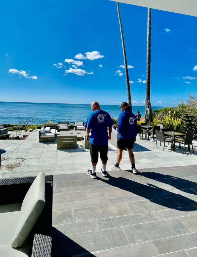 Two ASAP Movers crew members walking along a coastal walkway on a sunny day