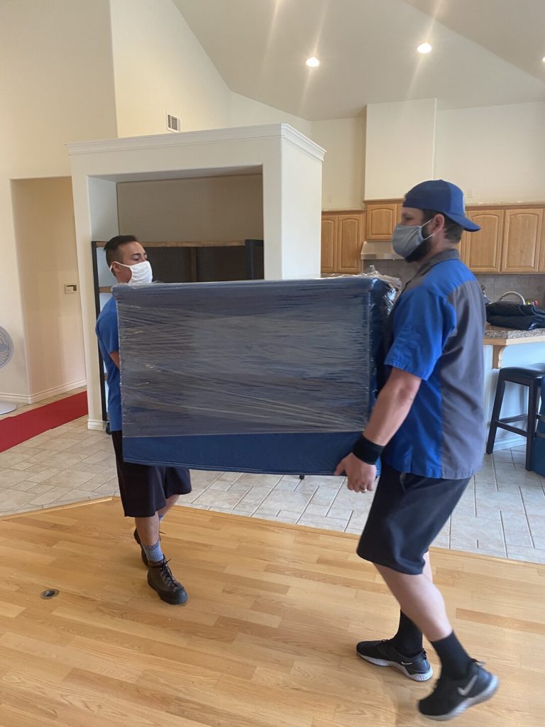 Two ASAP Movers crew members carrying a blanket-wrapped piece of furniture through a home